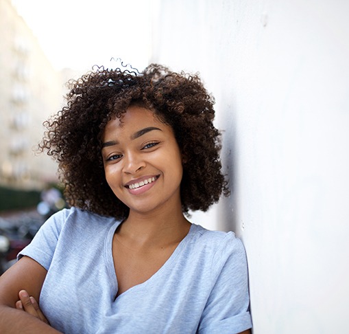 Woman in light blue shirt leaning against wall and smiling