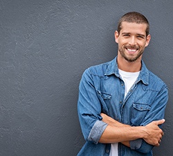 Man in denim jacket leaning against wall and smiling