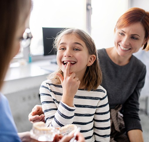 a young girl pointing to a missing tooth in a dental office