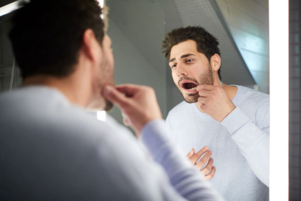 A man looking in the mirror at his teeth.