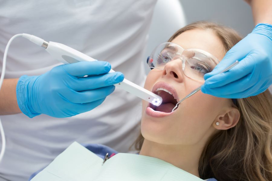 A dentist taking images of a woman's mouth with an intraoral camera.